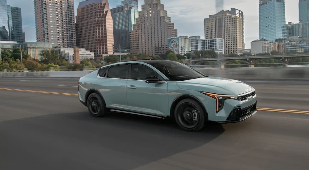 A light blue 2026 Kia K4 driving near a city.