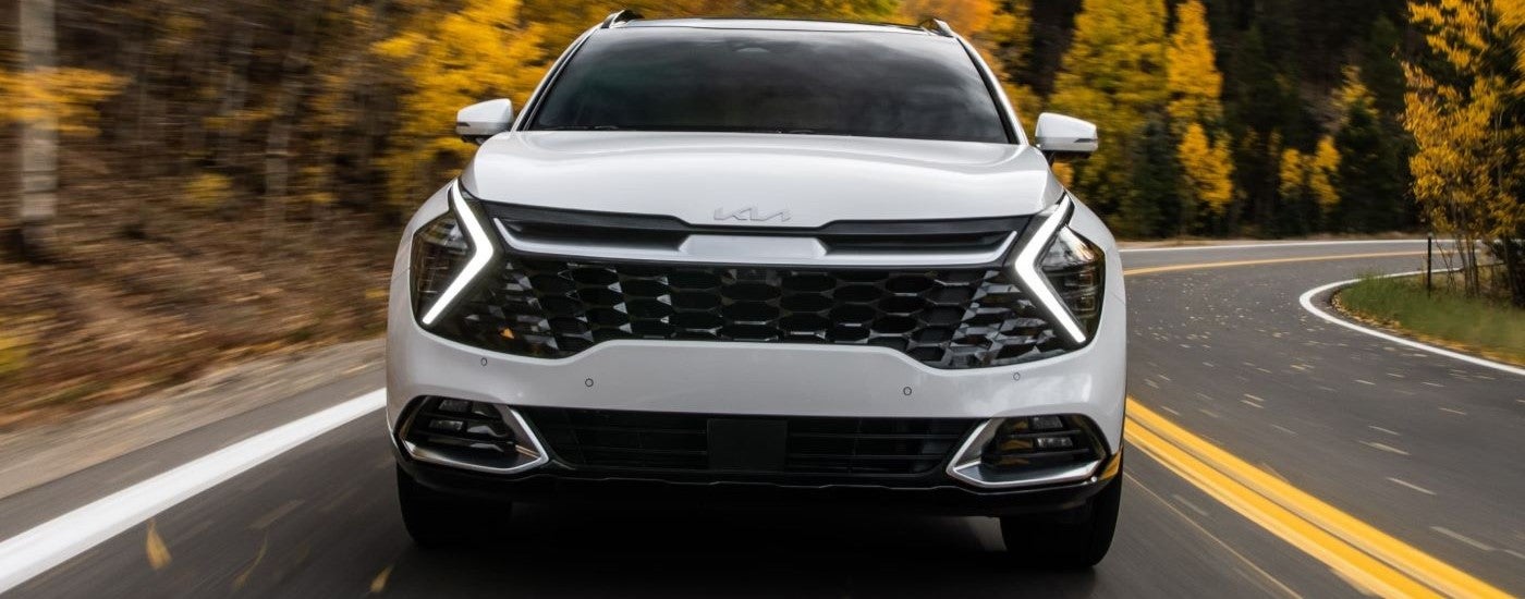Front of a white 2026 Kia Sportage driving on a road.