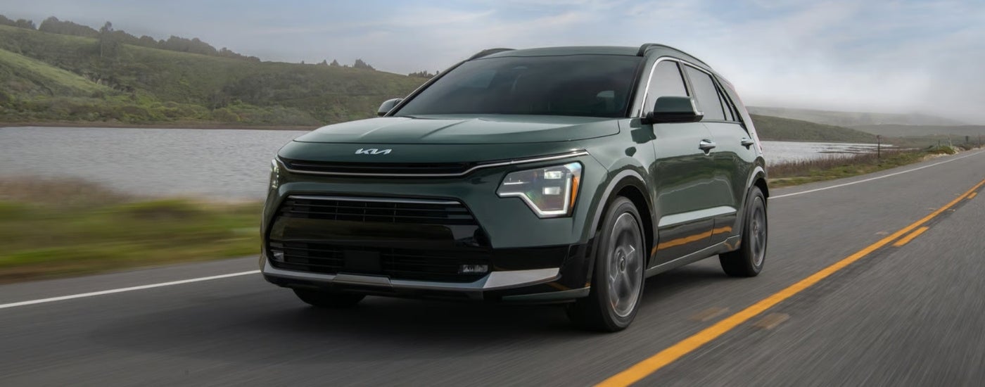 Green 2026 Kia Niro SX Touring driving on a road near a lake.