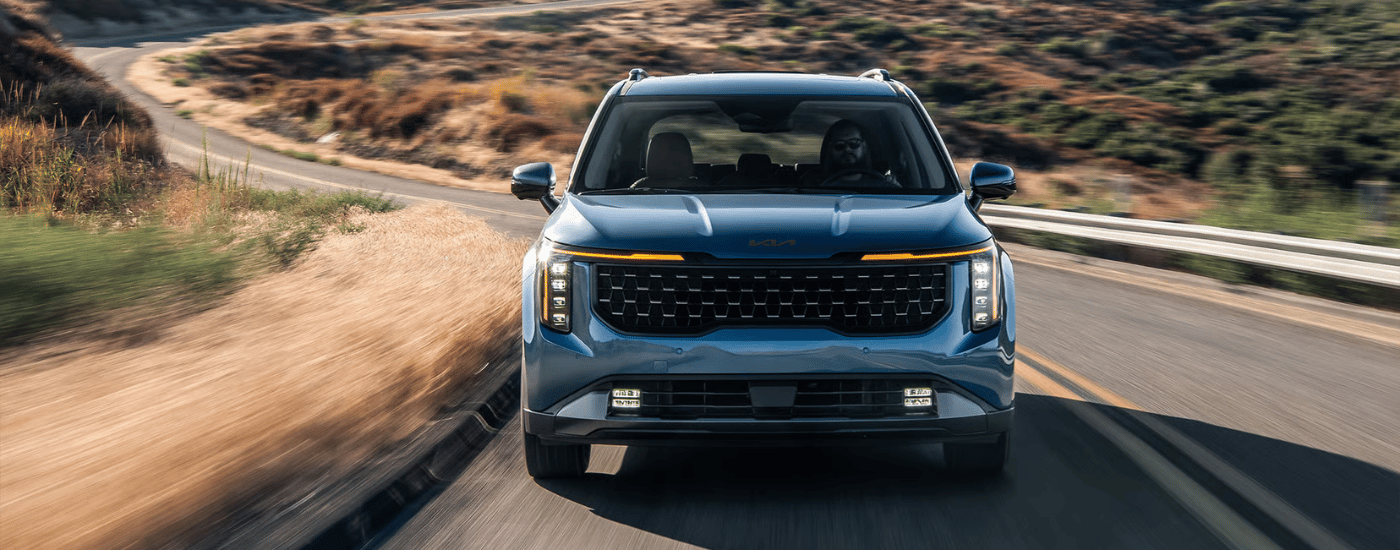 Blue 2026 Kia Carnival driving up an open road