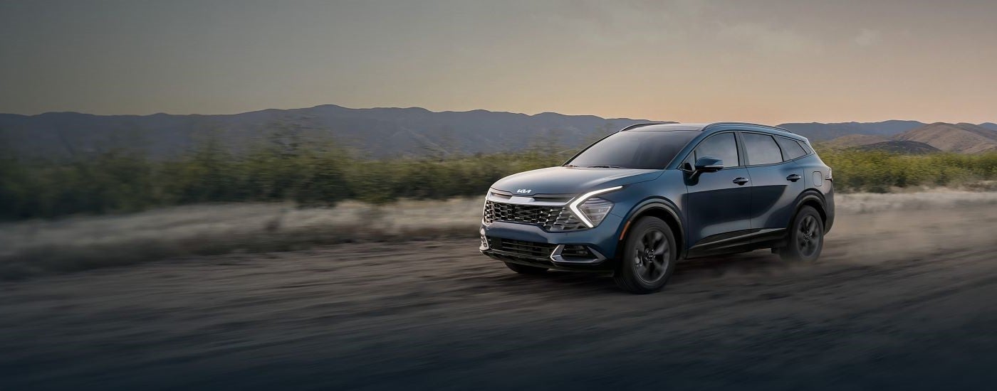Blue 2026 Kia Sportage driving down a dirt road.