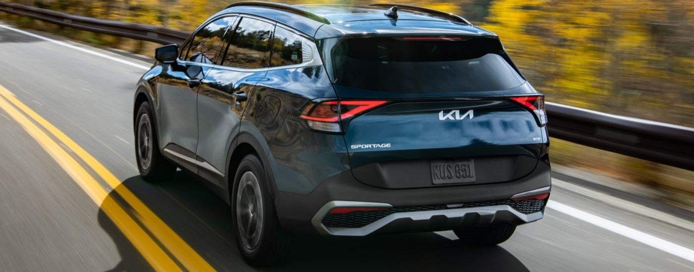 Rear of a blue 2026 Kia Sportage Hybrid driving down a road.