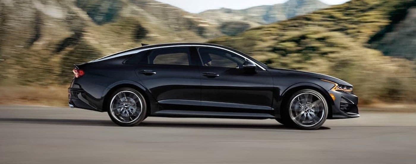 A black 2021 Kia K5 driving to a used Kia dealer.